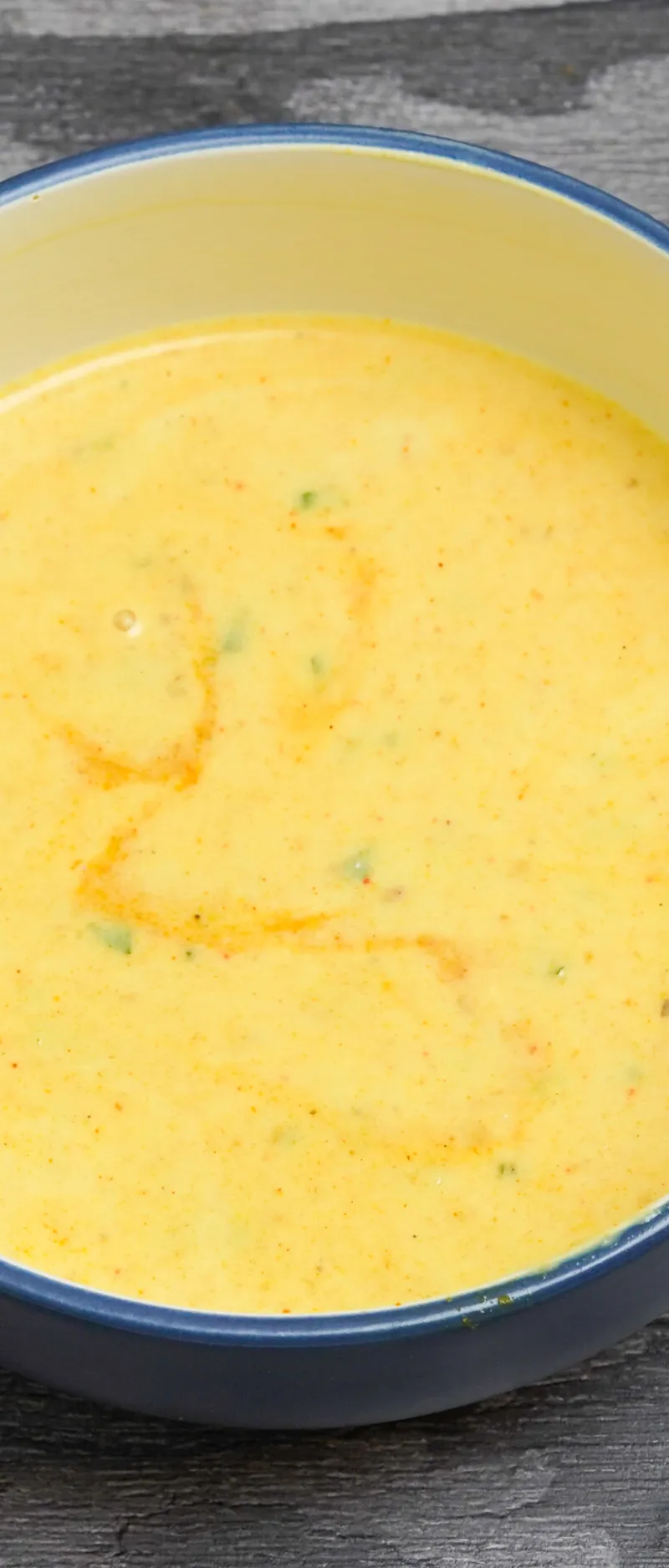 Round, blue and yellow bowl holding a creamy yellow curry or lentil dish speckled with herbs and spices.