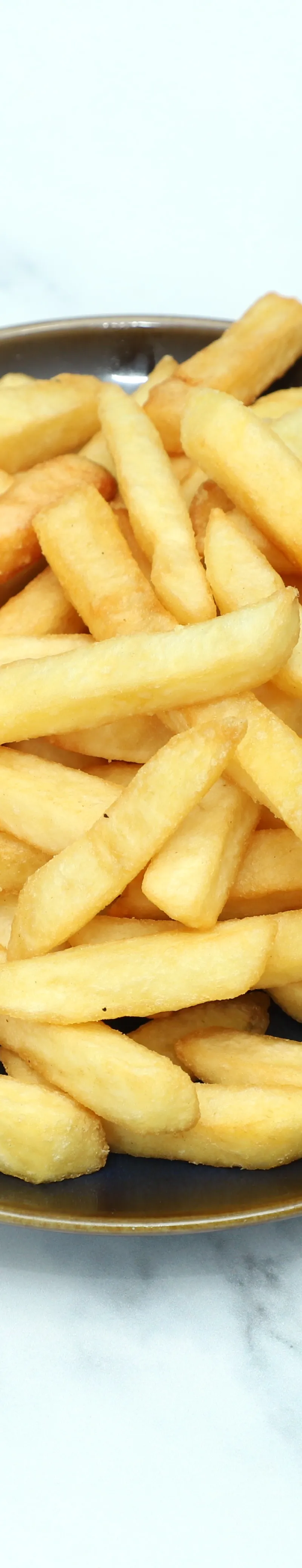 A round brown plate filled with golden crispy French fries resting on a white marble surface.