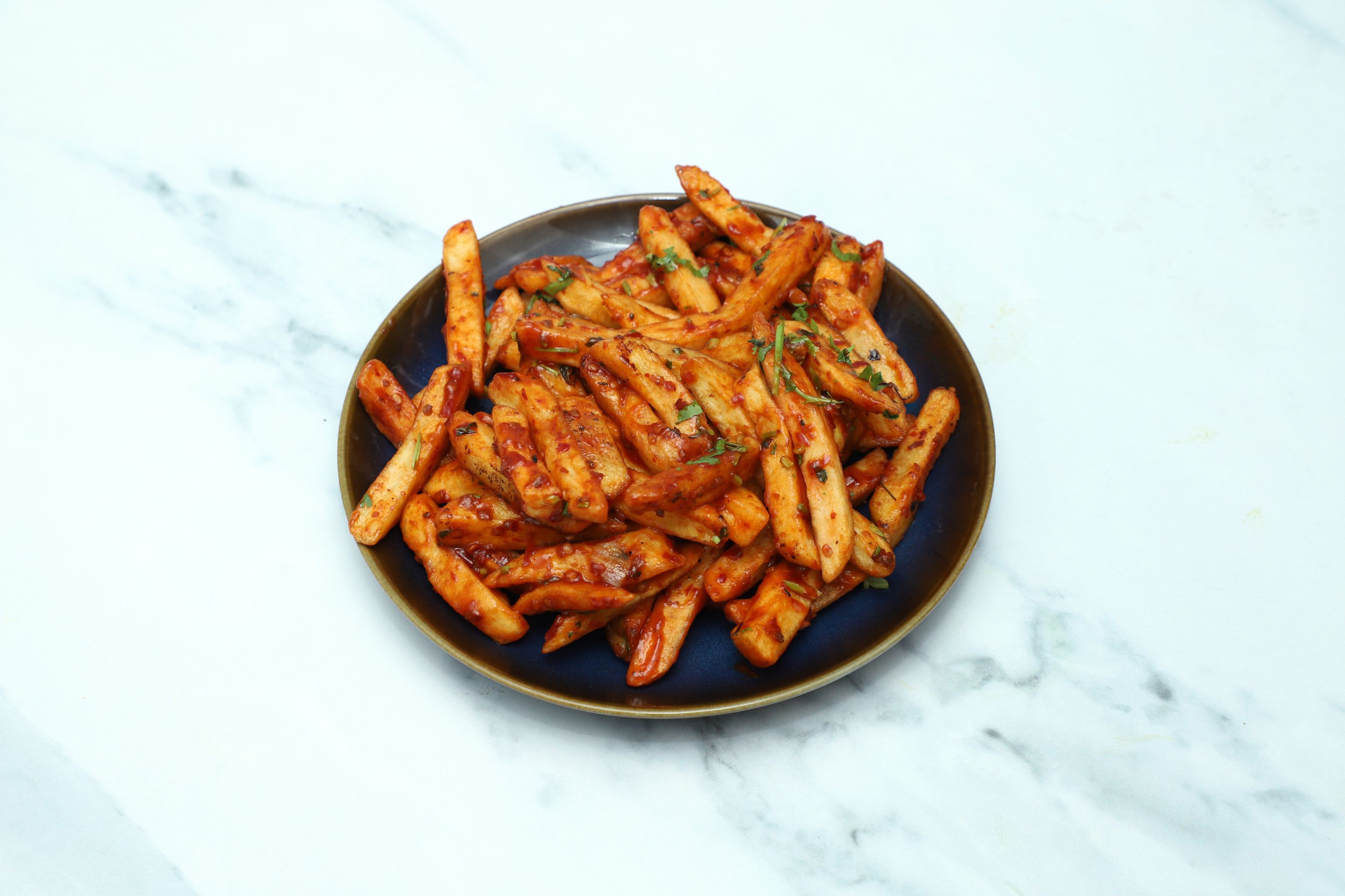 Delicious chilli chips coated in a spicy red sauce and topped with fresh coriander on a dark blue plate.