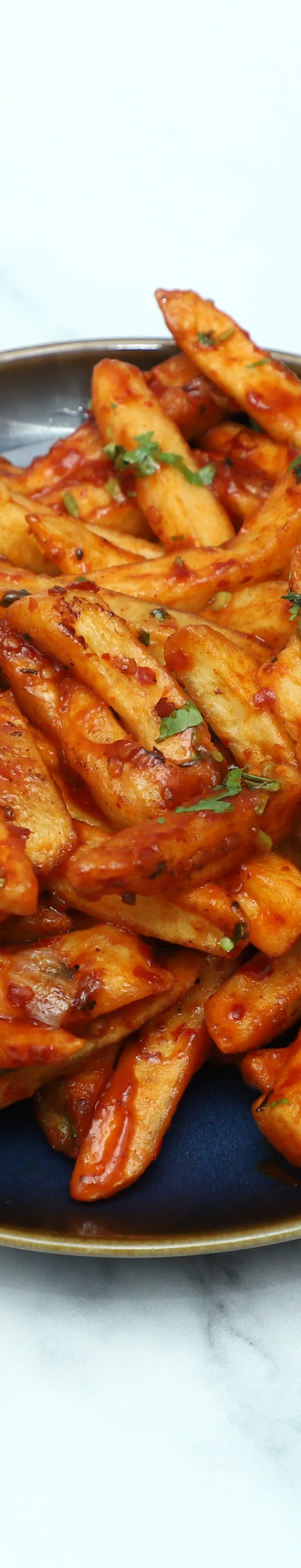 Delicious chilli chips coated in a spicy red sauce and topped with fresh coriander on a dark blue plate.