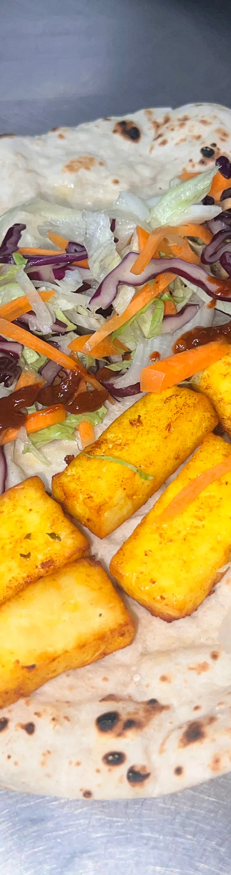 A flatbread wrap with golden fried paneer pieces, shredded lettuce, red cabbage, carrots, and a dark chutney.