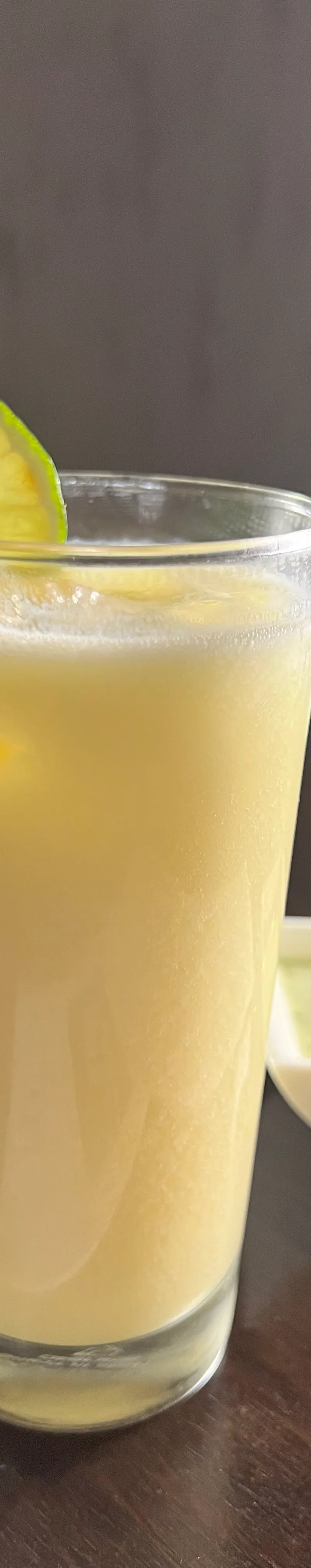 Mango lassi in a tall glass, garnished with a lime slice, next to a small bowl of green chutney.