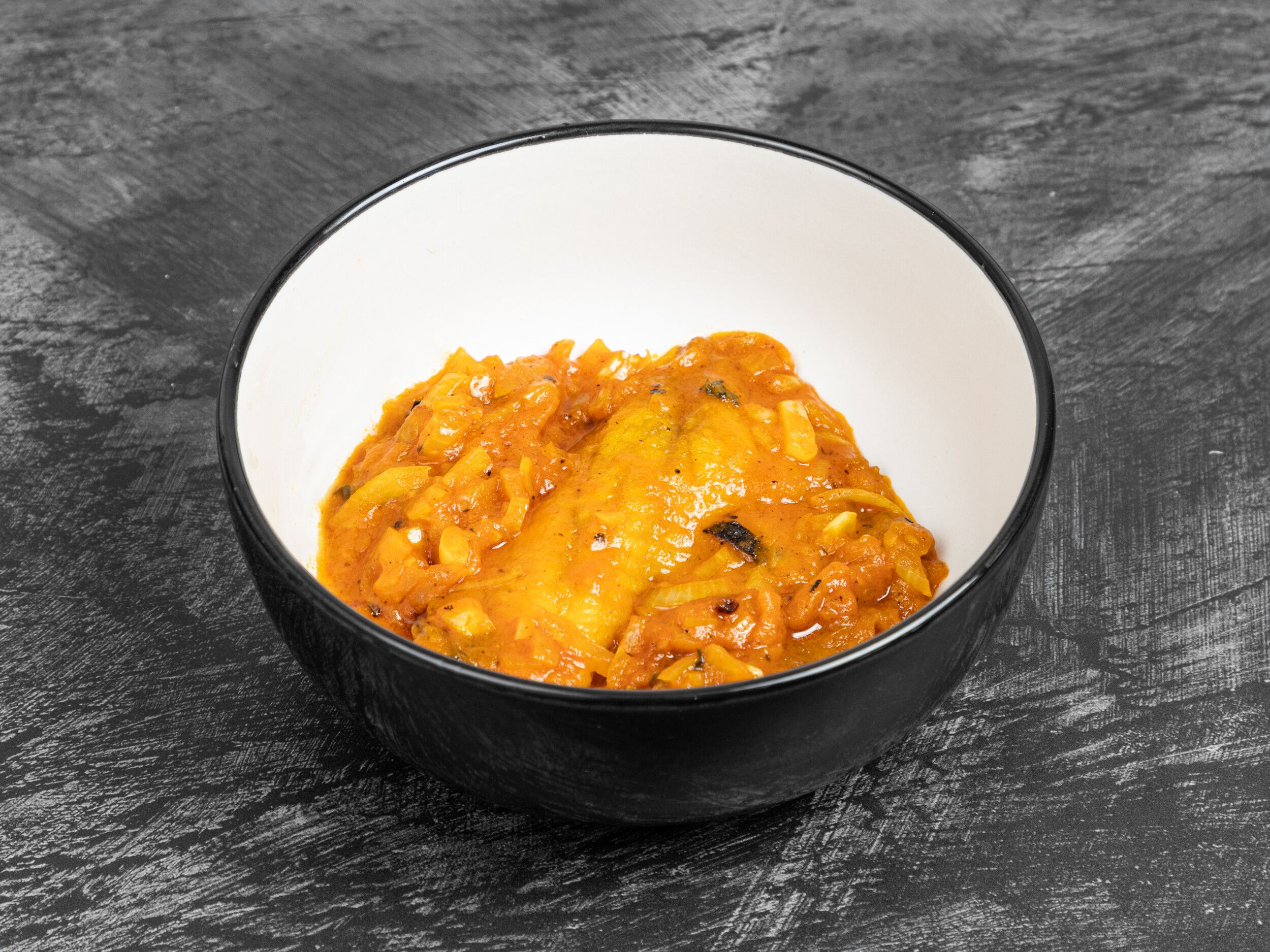 A close-up shot of a rich, orange-hued Indian curry with onions and spices in a white bowl with a black rim