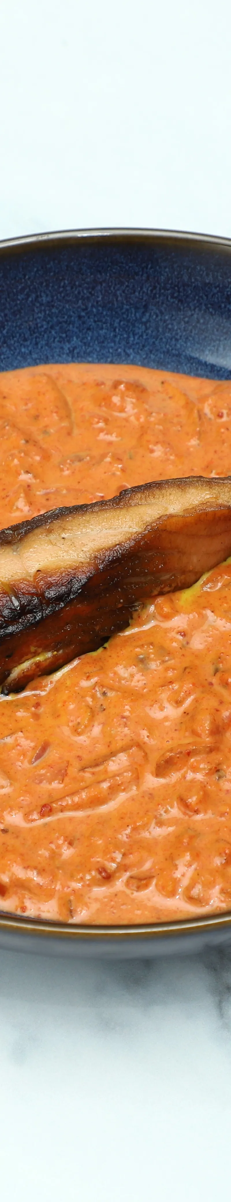 Grilled salmon fillet resting in a rich, creamy orange tomato-based curry in a blue bowl